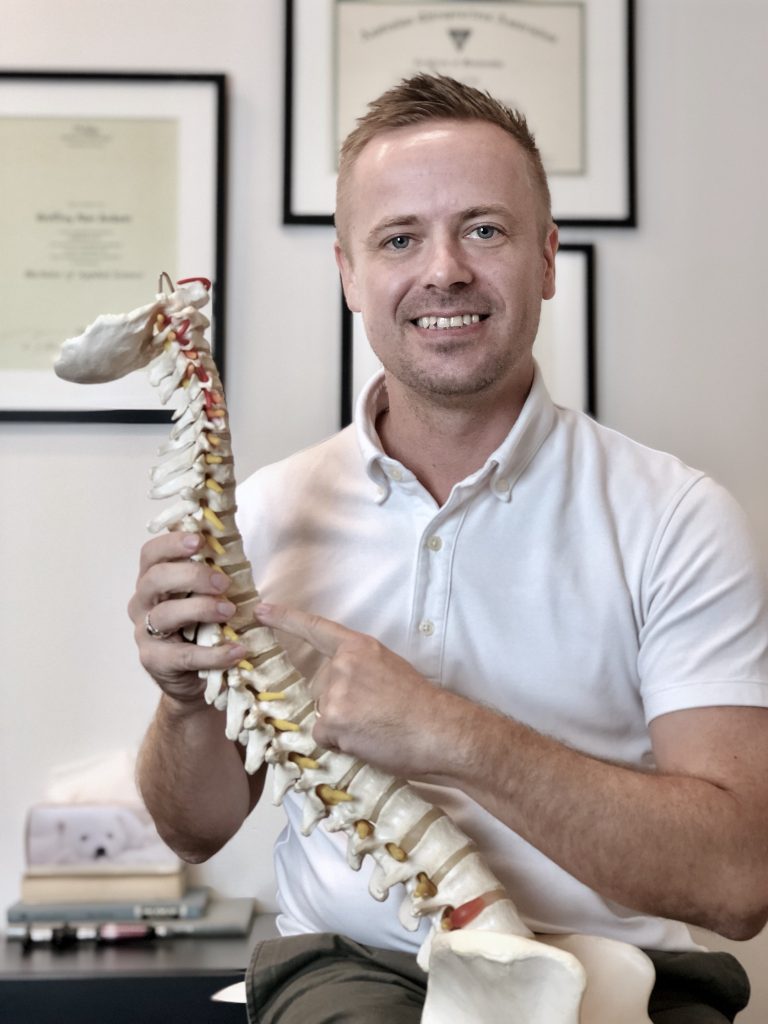 Dr Sam Fitzgibbons chiropractor wearing a white shirt and holding a spine model